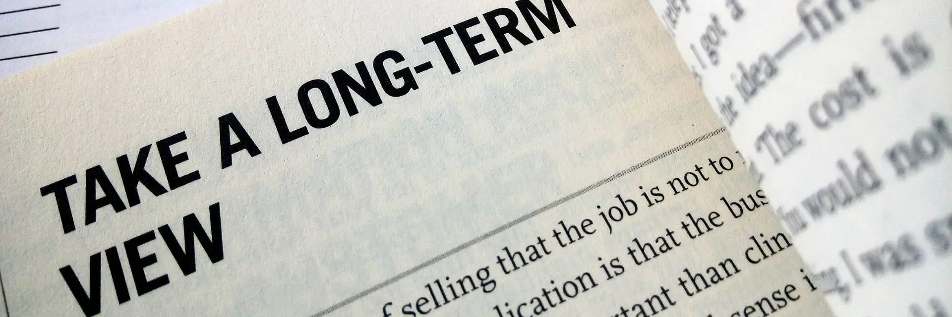 Nahaufnahme eines aufgeschlagenen Buches mit der prägnanten Aufschrift ‚TAKE A LONG-TERM VIEW‘ – Symbol für strategische Weitsicht und nachhaltige Selbstreflexion in der Führung.
