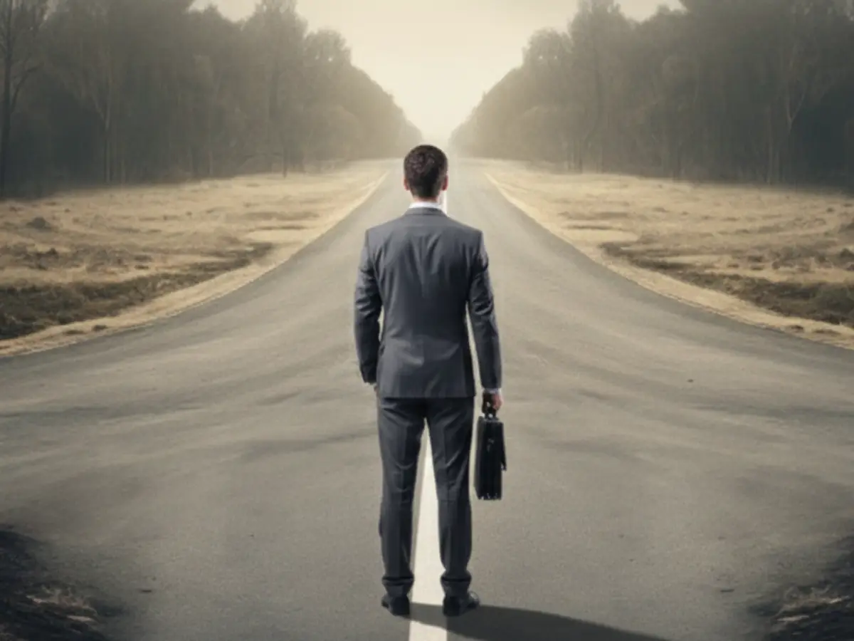 Orientierung: Geschäftsmann steht an einer Weggabelung auf leerer Straße vor zwei möglichen Wegen.