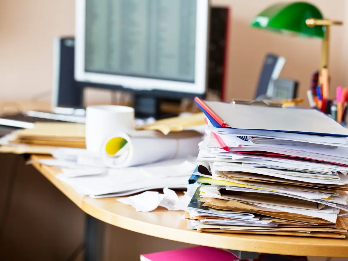 Unübersichtlicher Schreibtisch voller Unterlagen und Akten, der die systematische Vermeidung klarer Prioritäten im unternehmerischen Alltag symbolisiert.